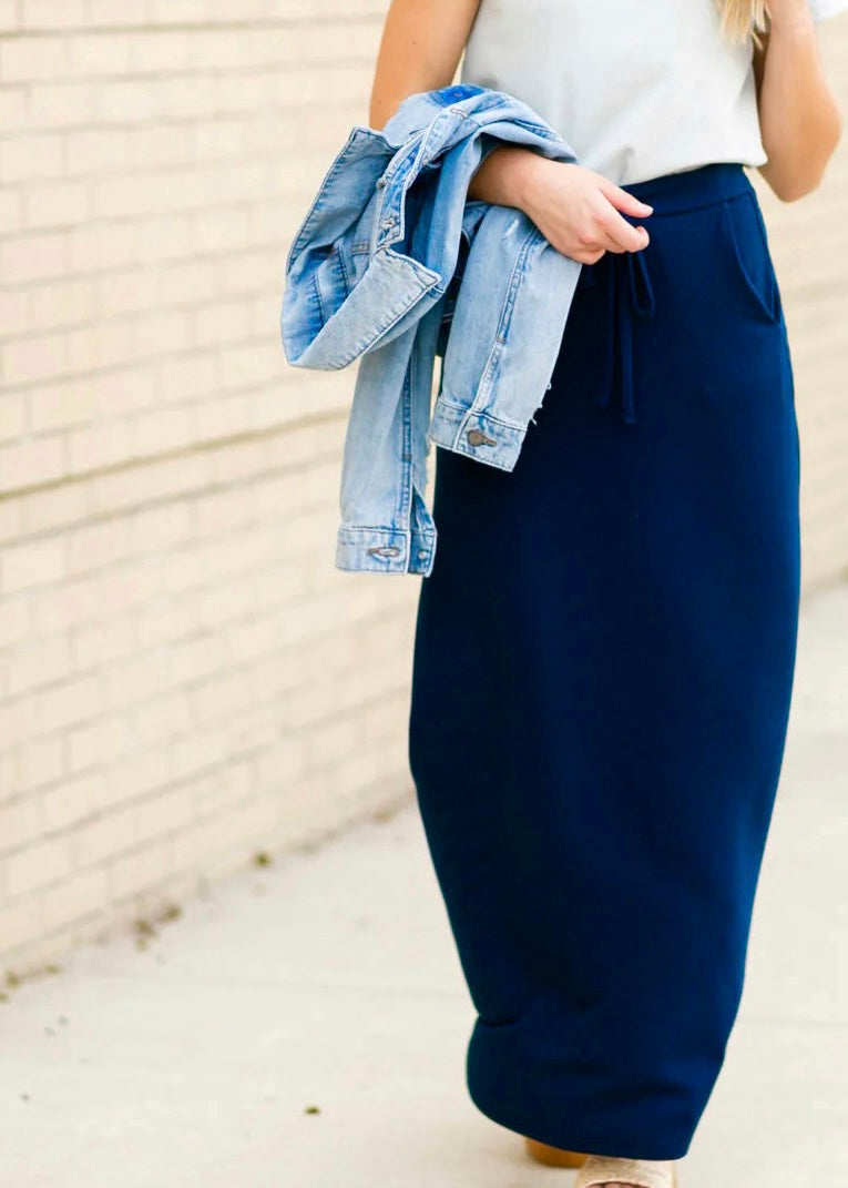Bottom half view of a young woman wearing a navy blue Maxi Skirt with Pockets featuring a Soft & Stretchy Premium Fabric Blend, Adjustable Drawstring Tie Waist, and Pockets. Available in sizes S-3XL in both solid Black or Navy Blue. Discover our Best Selling All-year All-season Maxi Skirt for every body shape & size.