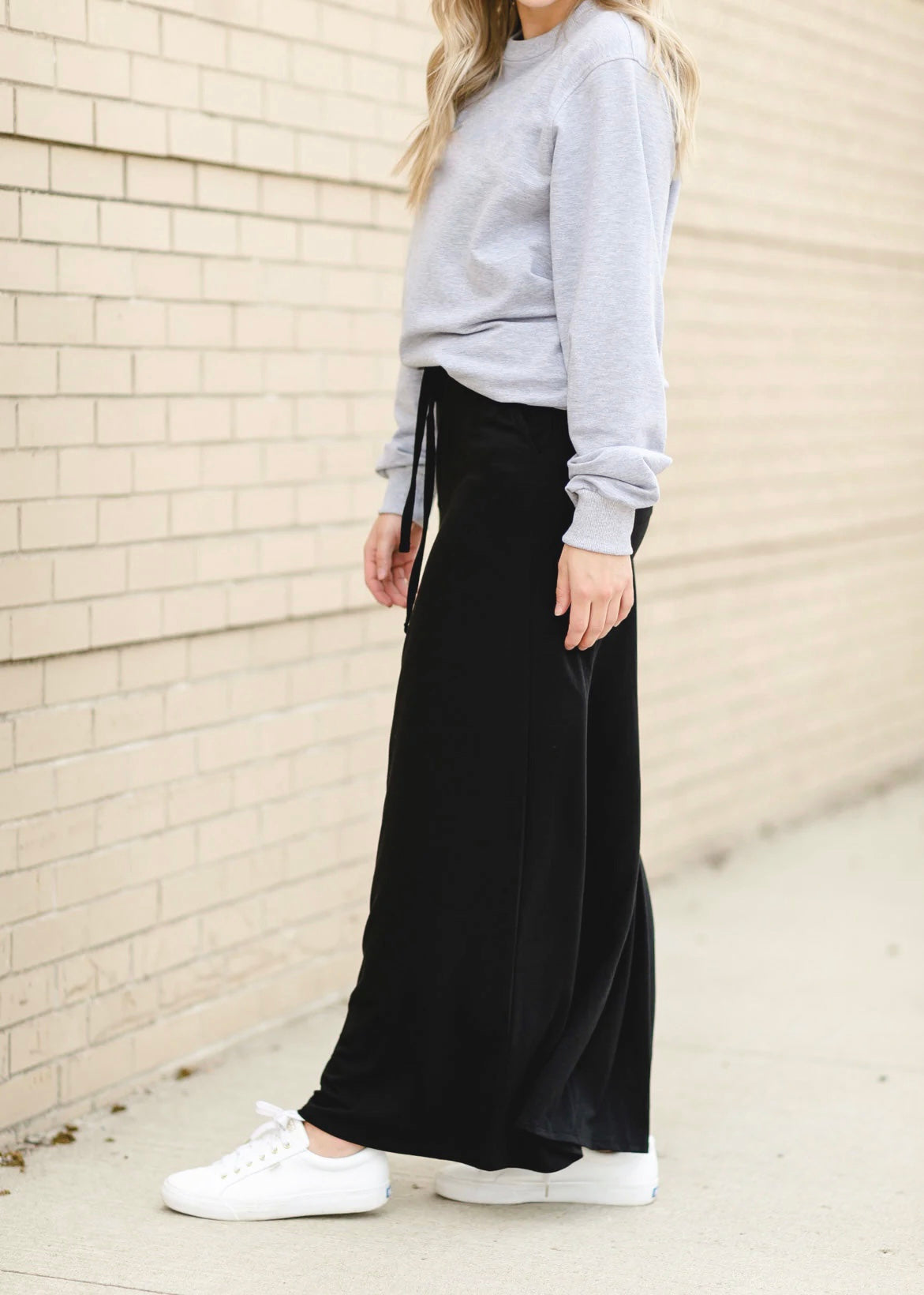 Bottom half view of a young woman wearing a solid black Maxi Skirt with Pockets featuring a Soft & Stretchy Premium Fabric Blend, Adjustable Drawstring Tie Waist, and Pockets. Available in sizes S-3XL in both solid Black or Navy Blue. Discover our Best Selling All-year All-season Maxi Skirt for every body shape & size.