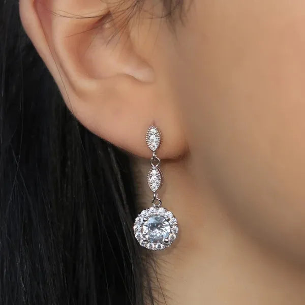 When only the extraordinary will do, choose The Trinity Embraced Solitaire Drop Earrings. Featuring a round solitaire nestled in a 4-prong circular cluster setting cascading from a duo of oval adornments.   Material: 925 sterling silver rhodium-plated  Length: 1.25"  Solitaire: 2 carat (1 carat per earring)  Weight: 0.2 oz (6 g) for set