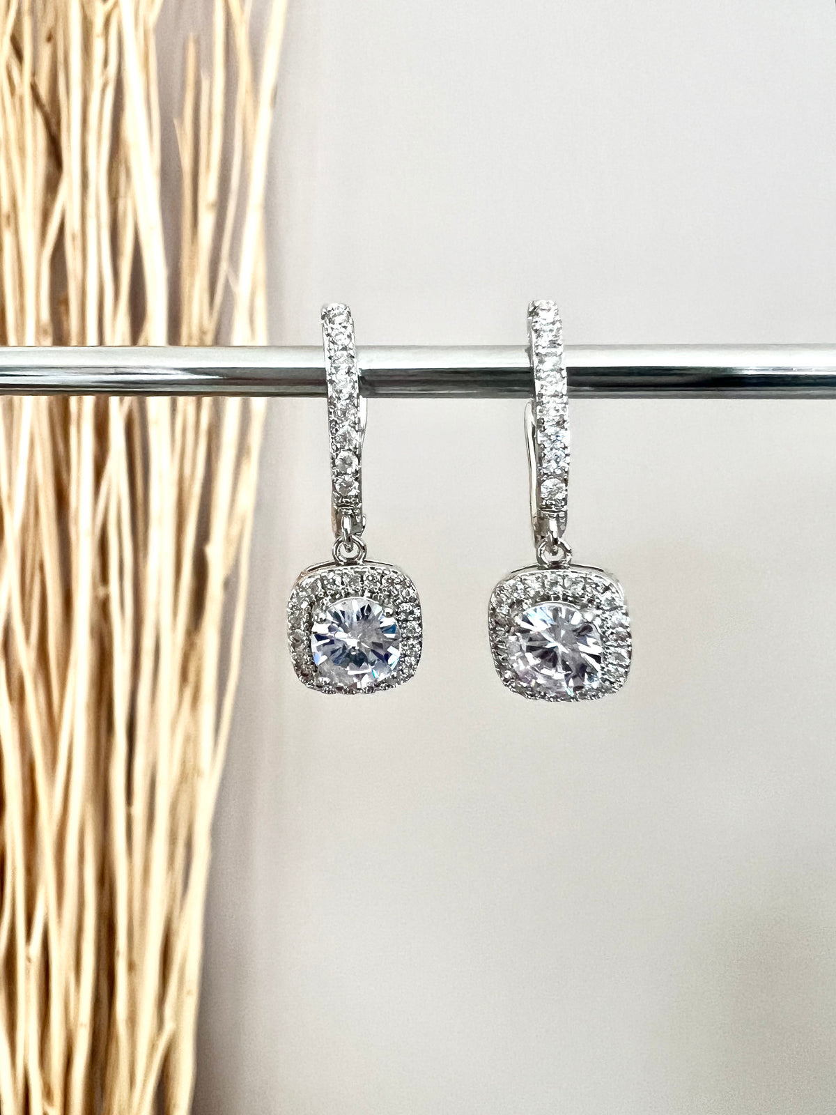 The Eleanor English Lock Embraced Solitaire Drop Earrings are crafted with a round solitaire in a square setting, secured by an English Lock Clasp for a secure fit. These earrings provide a timeless look with plenty of sparkle.   Material: 925 sterling silver rhodium-plated  Solitaire Cut: Brilliant Round  Setting: Halo Square Cushion  Length: 1"  Each earring: 1 carat  Total: 2 carat  Weight: 0.2 oz (6 g) for set