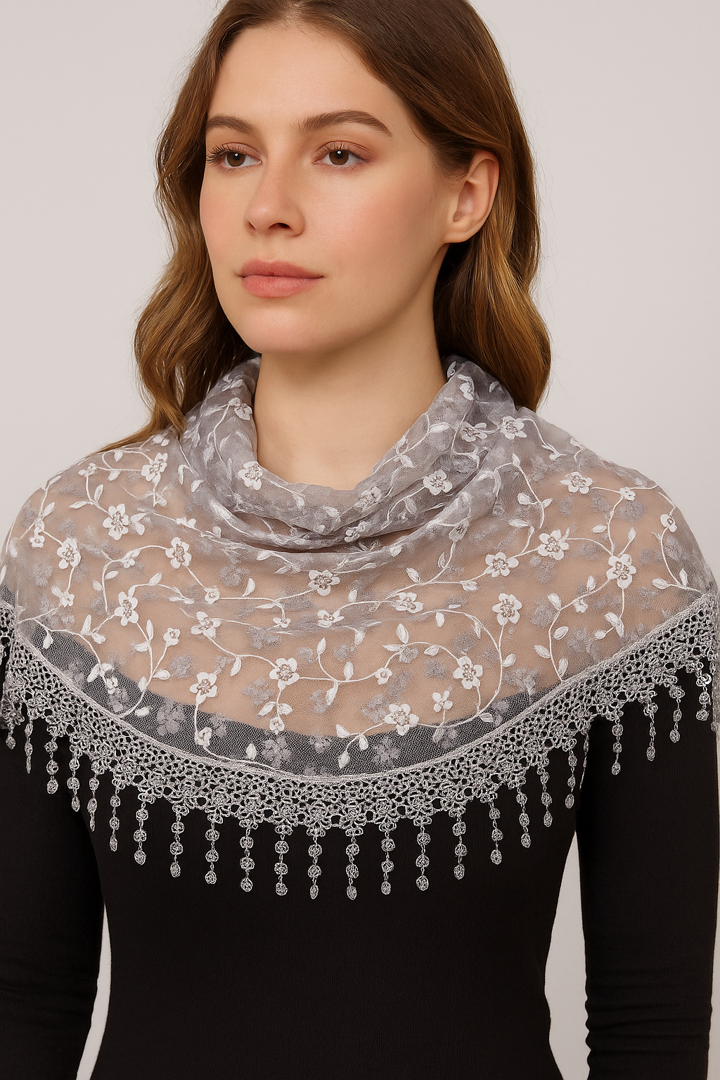 Woman wearing a floral lace grey silver scarf with tassels on a plain background