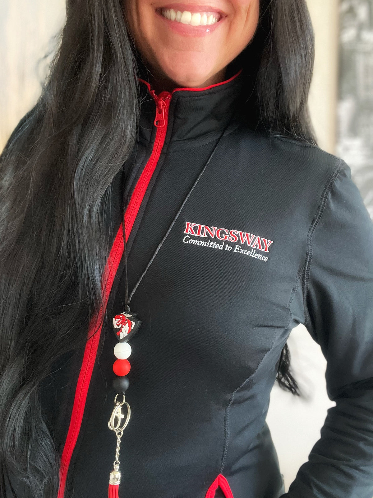 Smiling Woman with dark brown hair wearing a Kingsway Committed to Excellence Jacket and Dragon Lanyard with red Tassel and Black, White, and Red Silicone Beads and Lobster Clasp