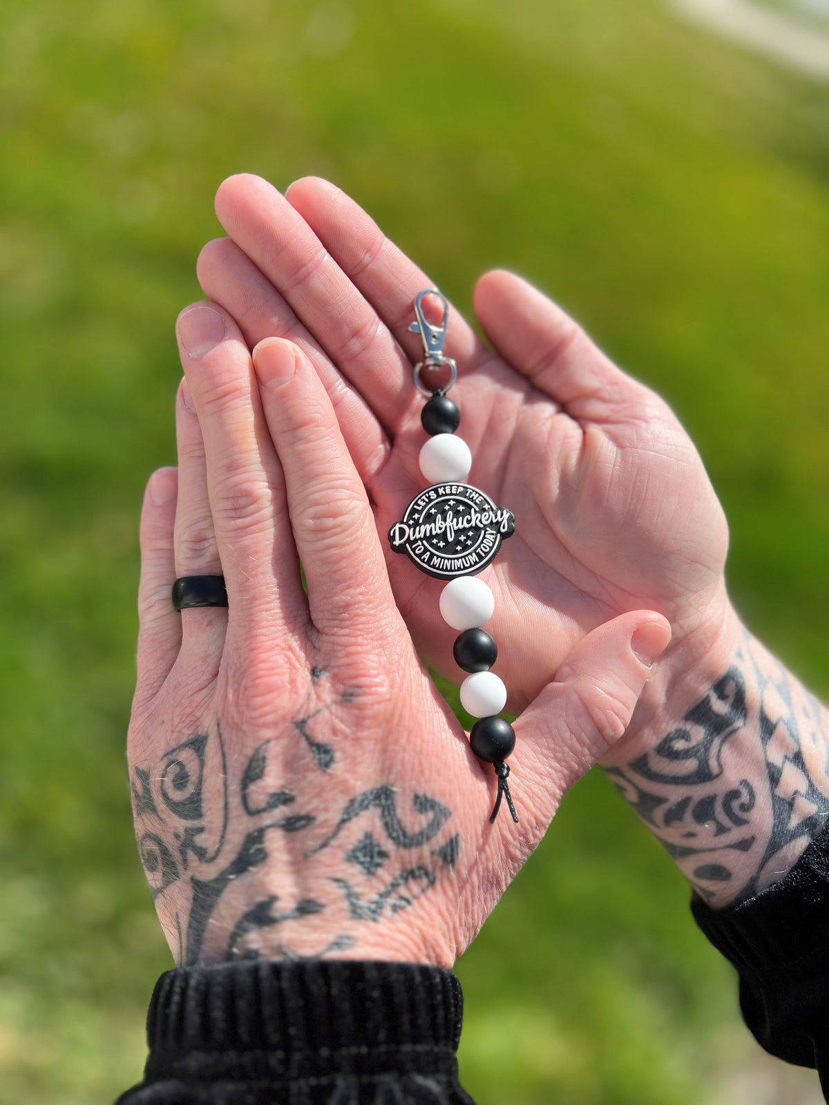 Tattooed mens hands holding a Black & White Let's Keep the Dumbfuckery to a Minimum Today Silicone Bead Keychain