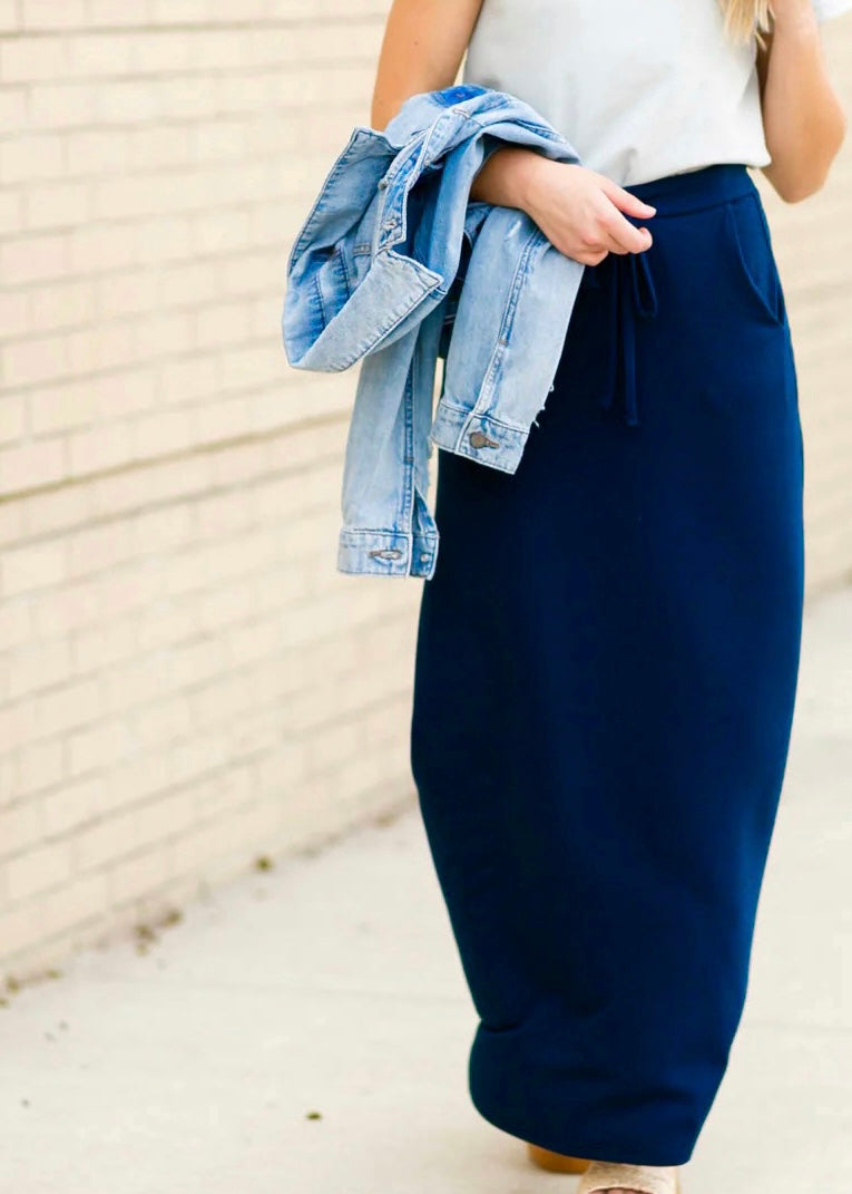 Bottom half view of a young woman wearing a navy blue Maxi Skirt with Pockets featuring a Soft & Stretchy Premium Fabric Blend, Adjustable Drawstring Tie Waist, and Pockets. Available in sizes S-3XL in both solid Black or Navy Blue. Discover our Best Selling All-year All-season Maxi Skirt for every body shape & size. 