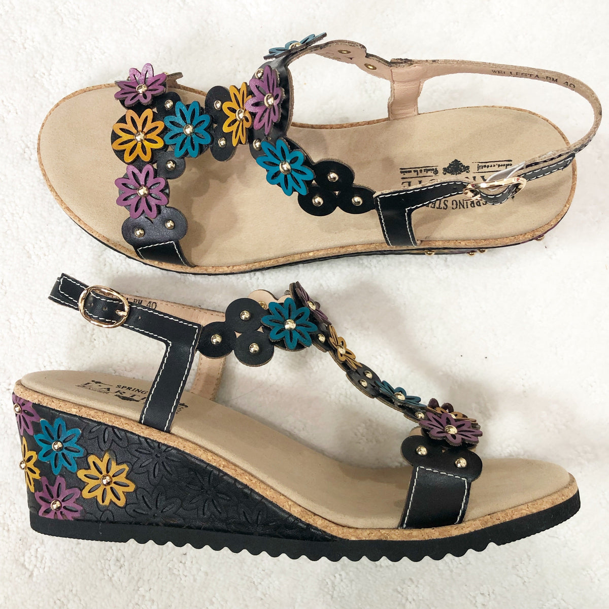 Stylish and comfortable T-strap leather wedge sandal called Wellesta by L'Artiste Springstep Footwear featuring a blend of geometrical and flowers detail upper dusted with round gold studs, a functional ankle straps buckle for adjustability and laser cut-out wrapped wedge with a cork trim edge.