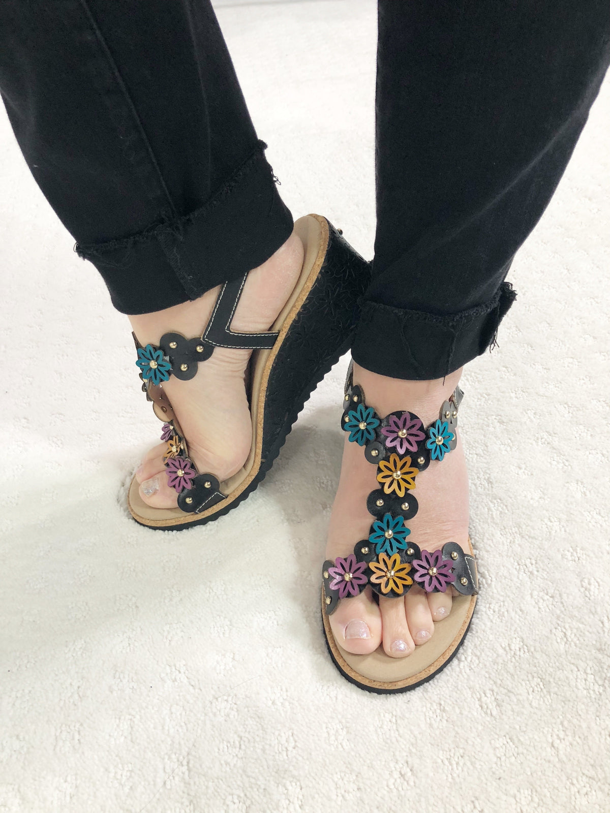Stylish and comfortable T-strap leather wedge sandal called Wellesta by L'Artiste Springstep Footwear featuring a blend of geometrical and flowers detail upper dusted with round gold studs, a functional ankle straps buckle for adjustability and laser cut-out wrapped wedge with a cork trim edge.