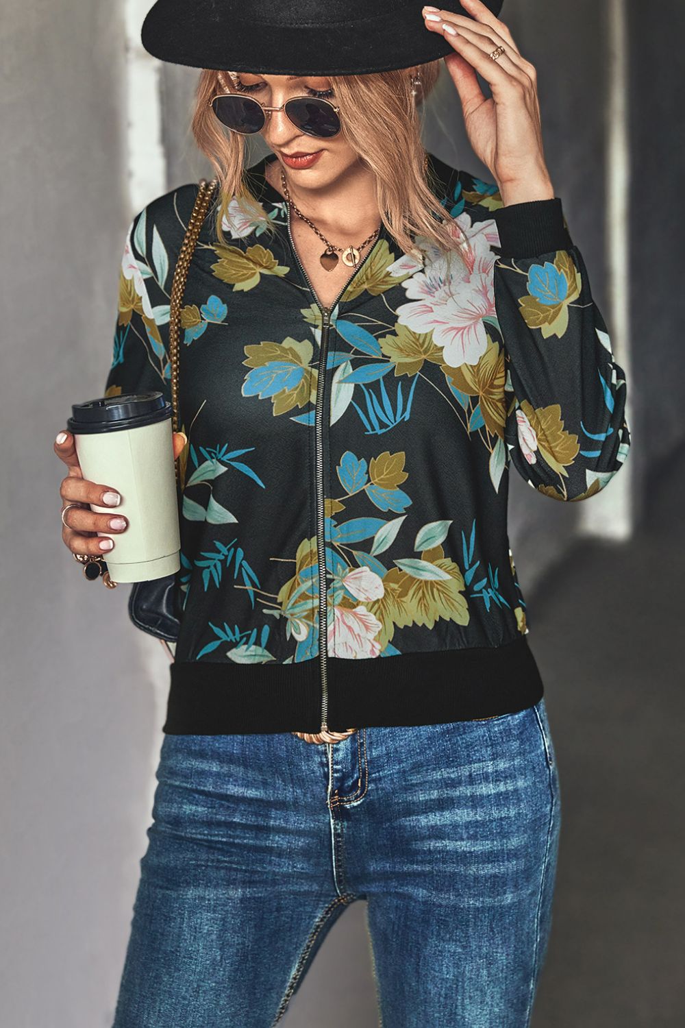 Blonde Woman wearing a black floral zip up lightweight floral bomber jacket with jeans