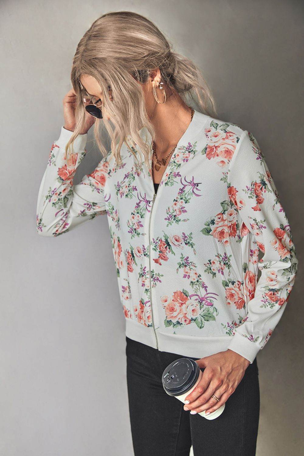 Woman wearing a white floral zip up lightweight floral bomber jacket with jeans