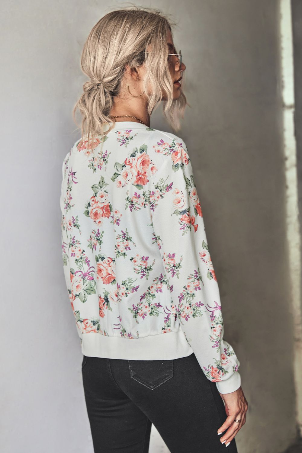 Woman wearing a white floral zip up lightweight floral bomber jacket with jeans
